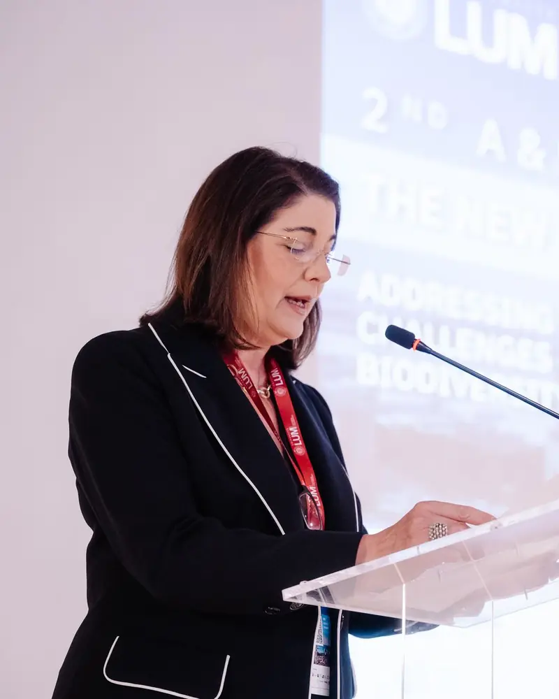 A speaker at the lectern, with the title of the 2nd A&F LUM Conference on the screen behind her.