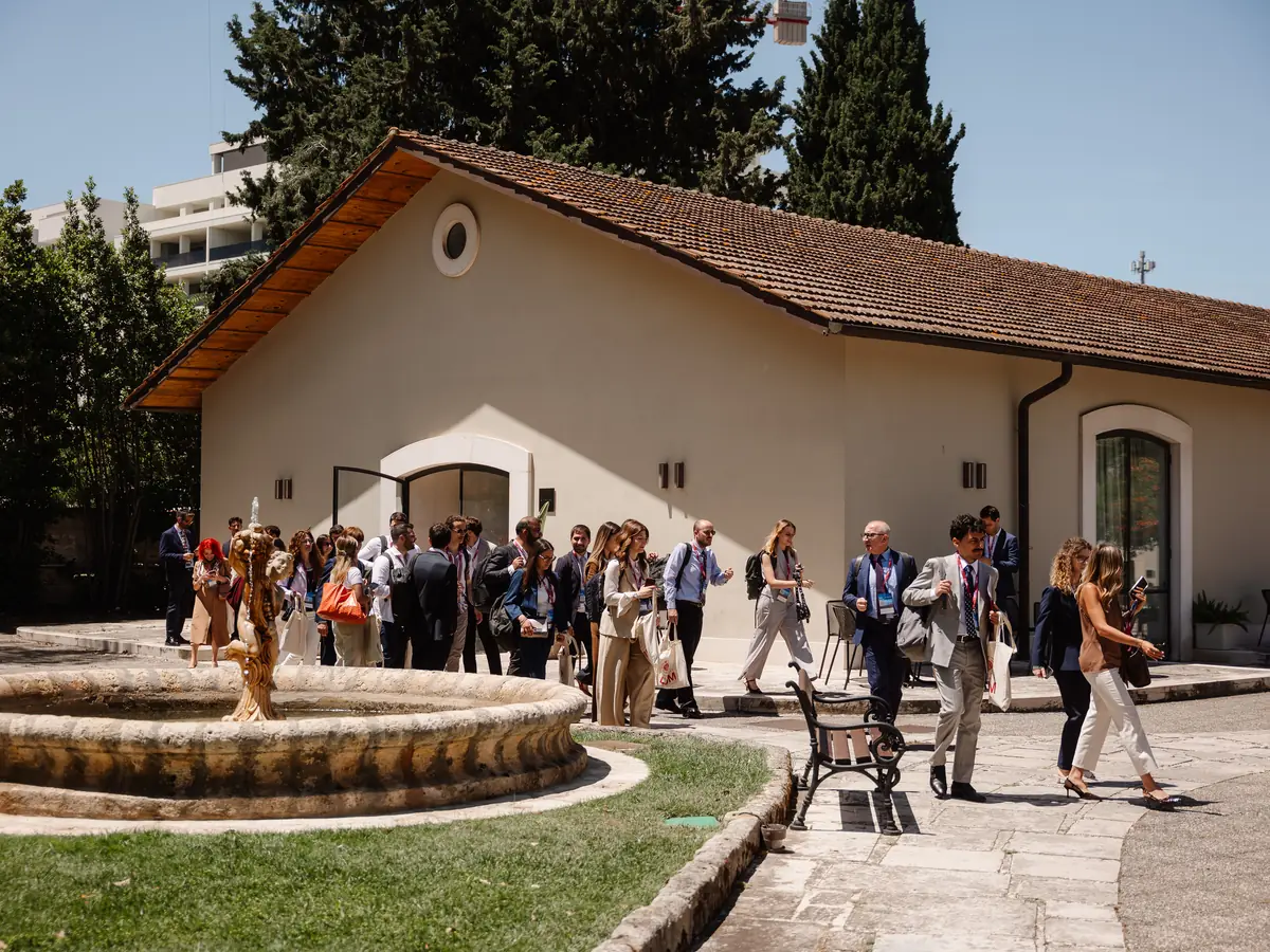 Conference participants walking through the park of Villa Romanazzi Carducci, beside one of its pavilions and a stone fountain.